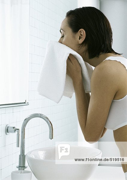 Frau steht über dem Waschbecken und trocknet Gesicht mit Handtuch