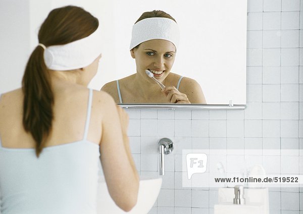 Frau beim Zähneputzen vor dem Spiegel im Bad