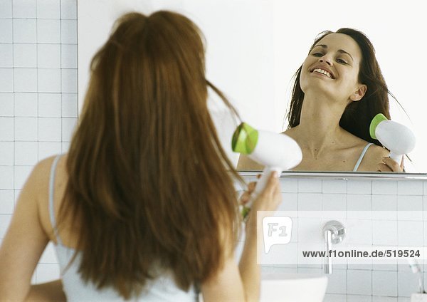 Frau trocknet Haare vor dem Spiegel