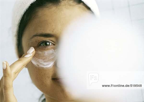 Frau  die Feuchtigkeitscreme unter dem Auge aufträgt  verschwommener Körper im Vordergrund
