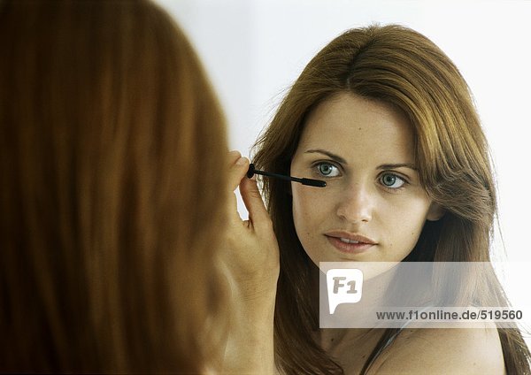 Frau beim Auftragen von Mascara im Spiegel