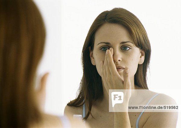 Woman applying moisturizer in mirror