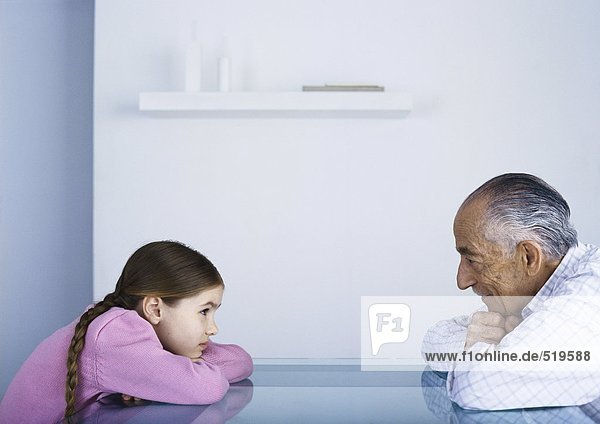 Großvater und Enkelin von Angesicht zu Angesicht am Tisch  die Köpfe ruhen auf den Armen.