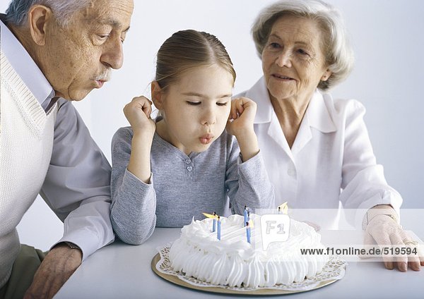 Mädchen sitzend mit Großeltern  Kerzen ausblasen auf Kuchen