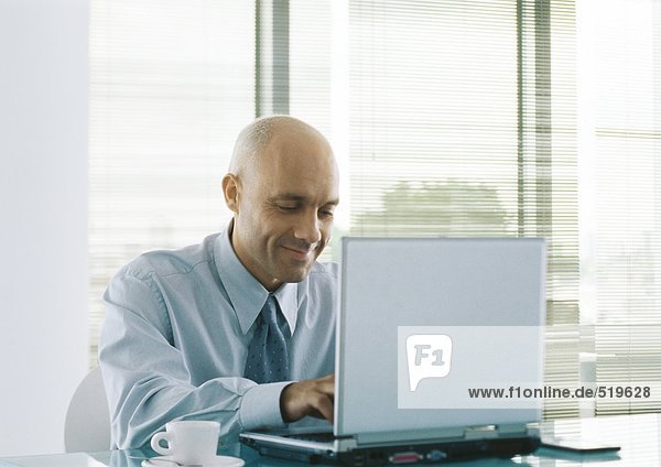 Businessman using laptop  smiling  coffee cup beside him on table