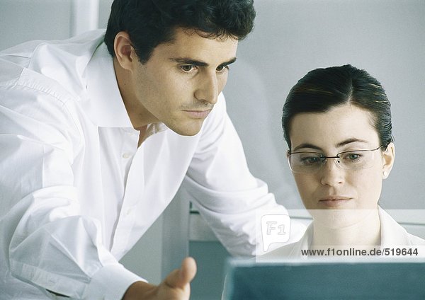 Woman working at computer  male colleague leaning over shoulder  gesturing to screen