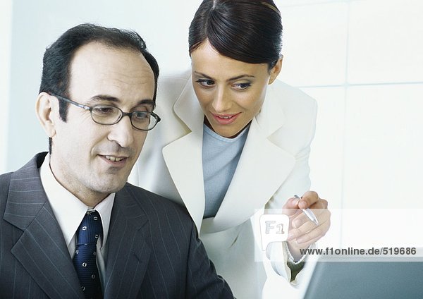 Businesswoman leaning over businessman's shoulder  pointing