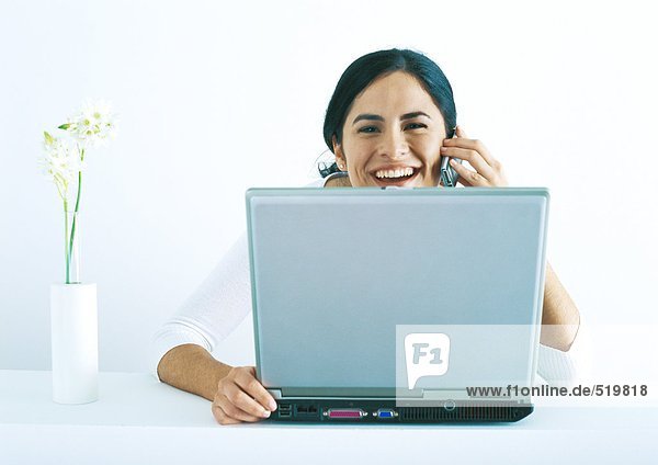 Frau sitzend mit Laptop  telefonierend und lachend