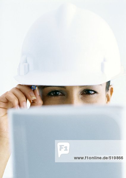 Woman wearing hard hat  looking over computer screen