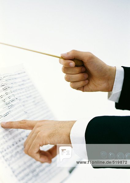 Dirigentenhände halten den Taktstock und zeigen auf Noten.