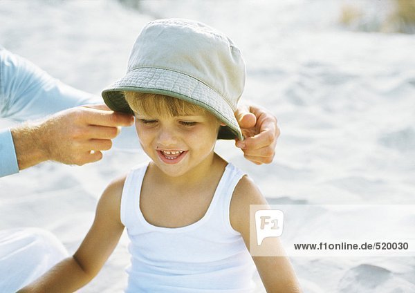 Vaters Hände setzen Hut auf kleinen Jungen  am Strand