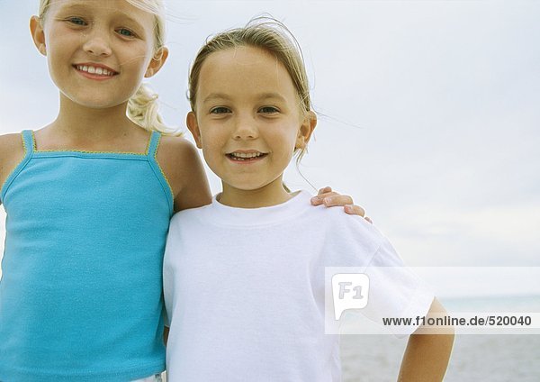 Zwei kleine Mädchen stehen Seite an Seite am Strand.