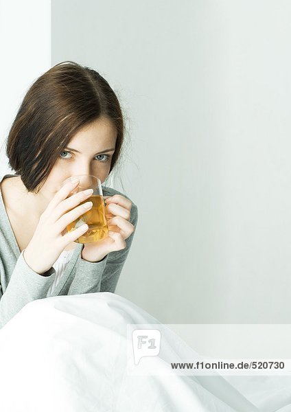 Junge Frau sitzt unter der Decke und trinkt heißen Tee.