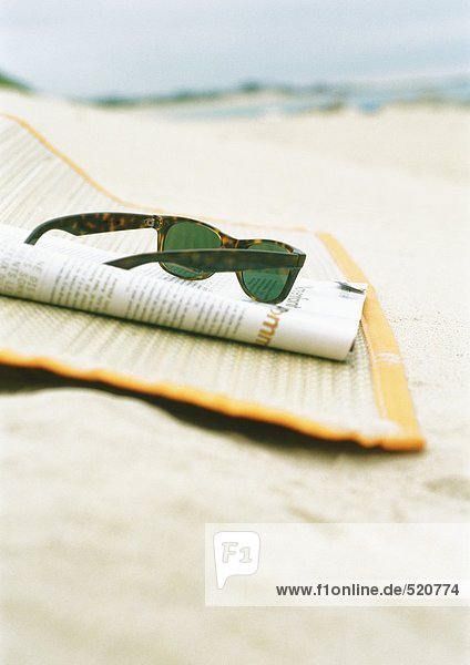 Sonnenbrille und Magazin auf Strandmatte