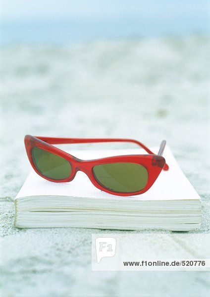 Sonnenbrille und Buch auf Sand
