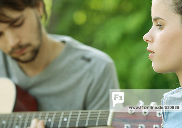 Young woman listening to young man playing guitar