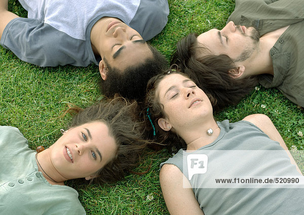 Vier Freunde liegen auf Gras mit Köpfen zusammen.