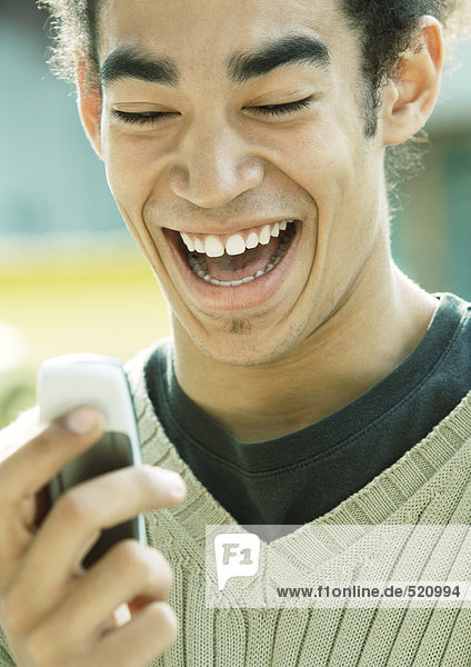 Junger Mann lacht und schaut aufs Handy  Nahaufnahme