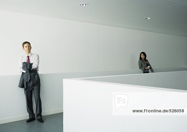 Geschäftsmann und Geschäftsfrau stehen getrennt im Bürogebäude