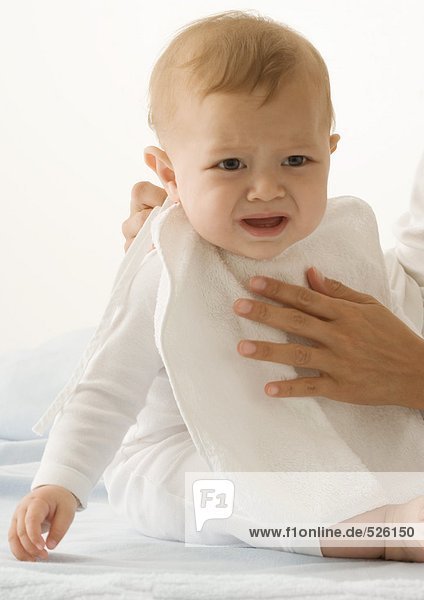 Parent putting bib on crying baby  cropped view