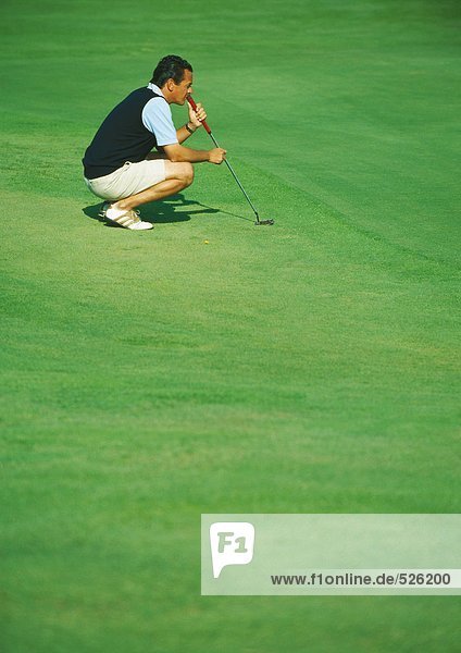 Golfer crouching on green