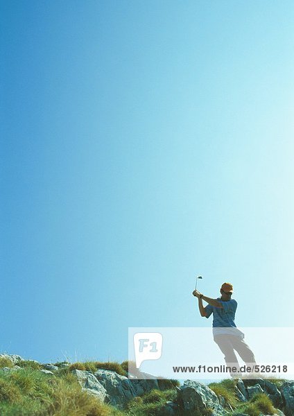 Golfer swinging on rugged terrain