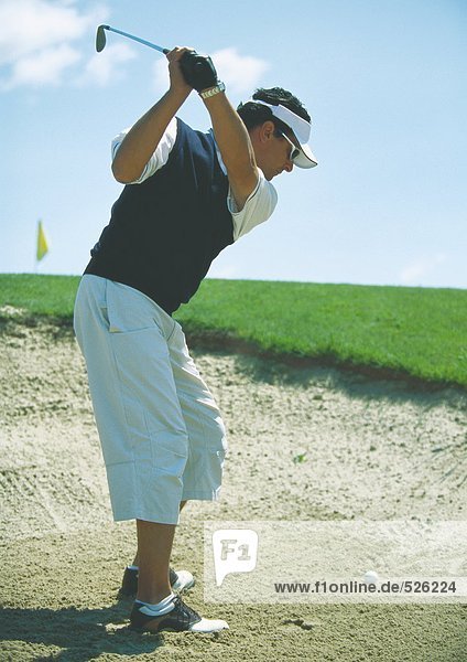 Golfer swinging in sand trap