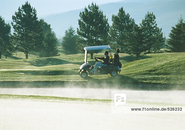 Golfer fährt Golfwagen neben Sandfang