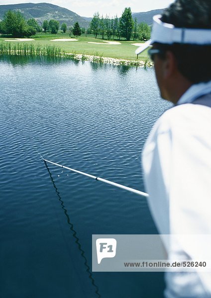 Golfer retrieving ball in pond with pole