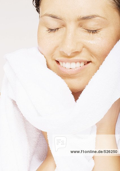 Frau lächelt mit geschlossenen Augen  wischt das Gesicht mit einem Handtuch ab.
