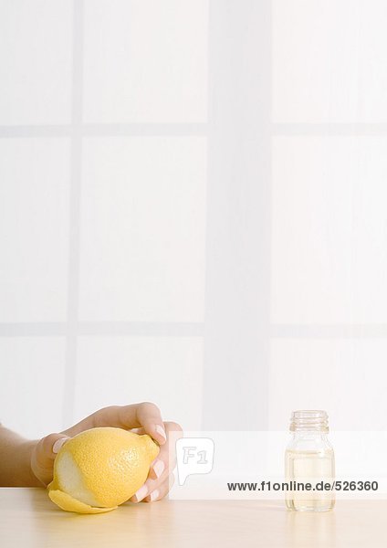 Frauenhand hält Zitrone neben Flasche ätherisches Öl