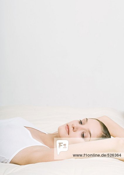 Frau auf dem Bett liegend mit den Armen über dem Kopf