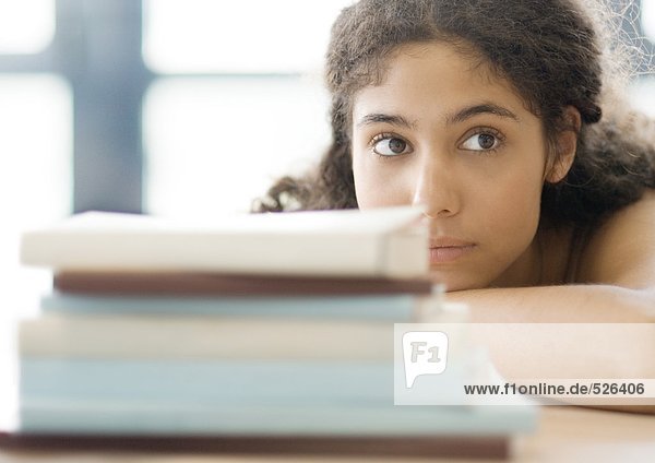 Young woman resting head on arms  behind pile of books