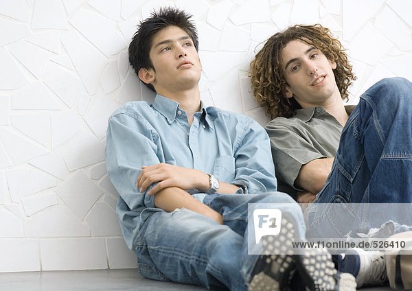 Two young men sitting on ground  leaning back against wall
