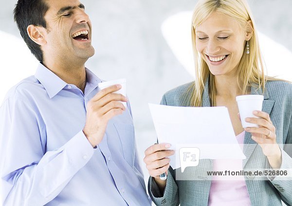 Businessman and businesswoman holding cups and laughing over document