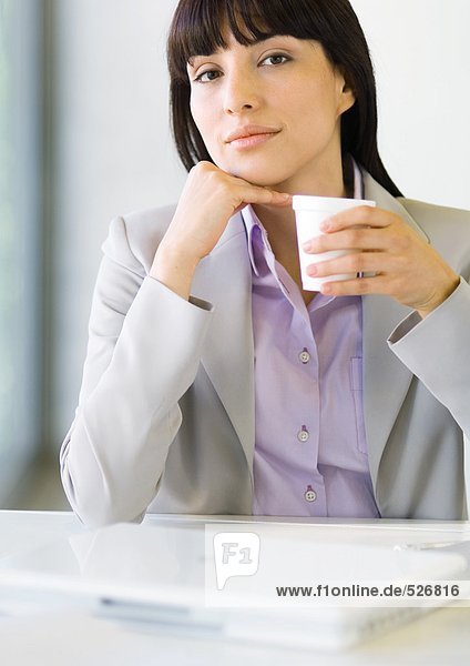 Geschäftsfrau am Schreibtisch sitzend  Tasse haltend