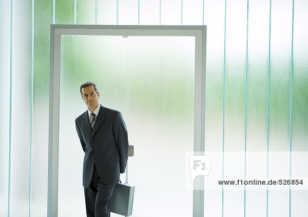Businessman standing in front of door  holding briefcase behind back