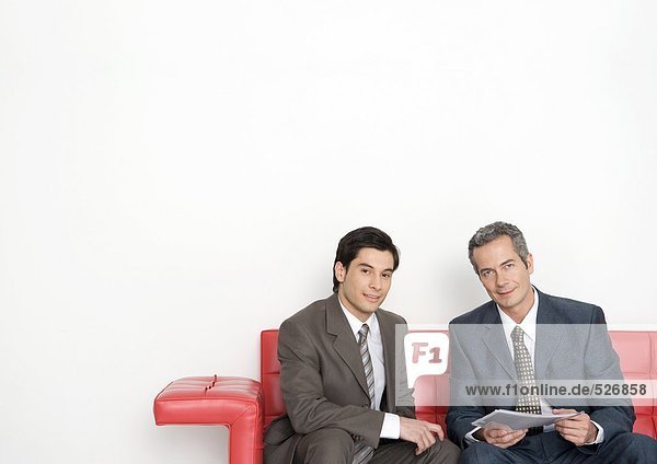 Zwei Geschäftsleute  die auf der Couch sitzen  einer davon hält ein Dokument.