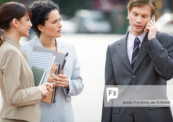 Businessman using cell phone while two female associates wait