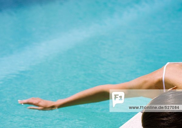 Frau neben dem Pool liegend mit der Hand auf der Wasseroberfläche