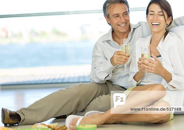 Adult couple sitting on floor  holding champagne flutes