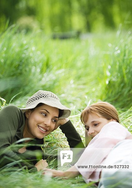Junge Frau und Mädchen liegen zusammen im Gras.