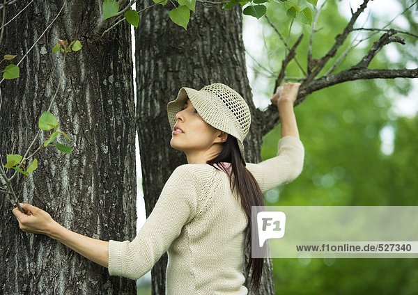 Junge Frau hält sich am Baum fest