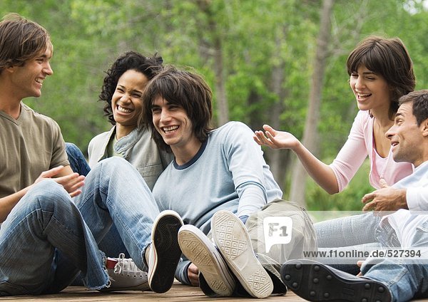 Gruppe junger Freunde  die zusammen im Freien sitzen und lachen.
