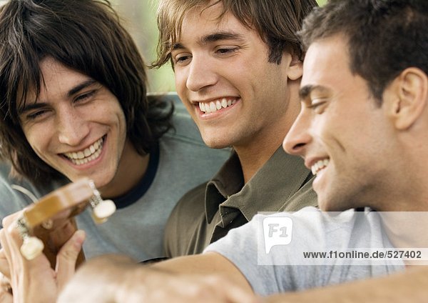 Three young male friends  looking at guitar