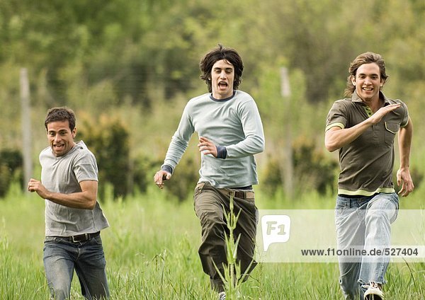 Three young male friends racing across field