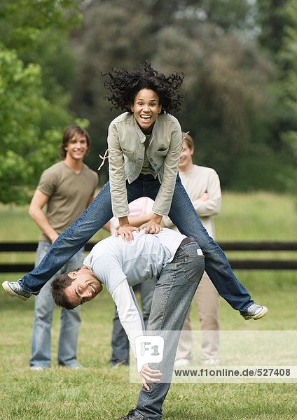 Young woman playing leapfrog with young man while friends look on