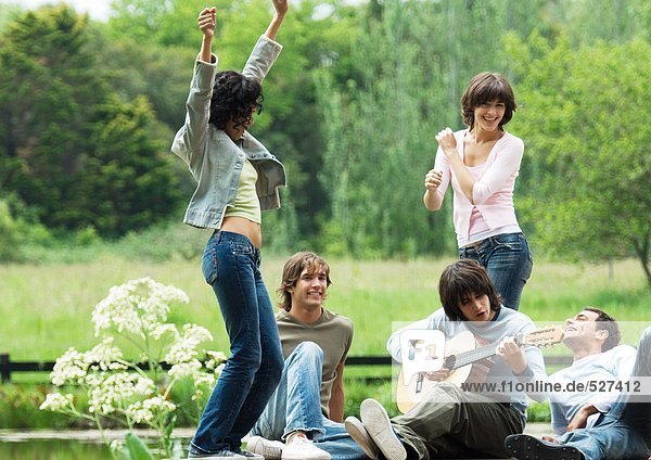 Group of friends outdoors  young women dancing while young man plays guitar
