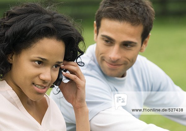 Junge Frau benutzt Handy  während der junge Mann zuhört.