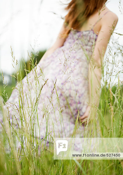 Junge Frau geht durchs Gras,  Kleid bläst im Wind